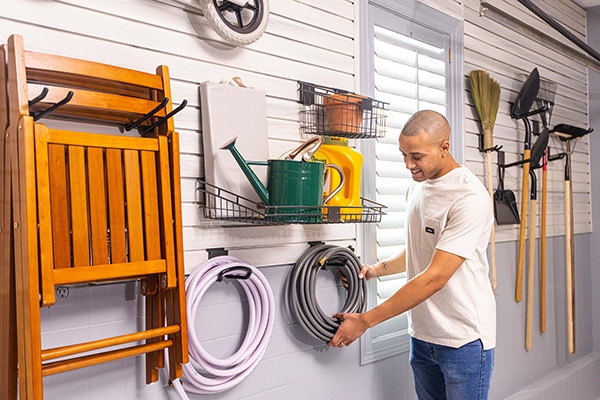 Man hanging up hoses on wall storage hooks