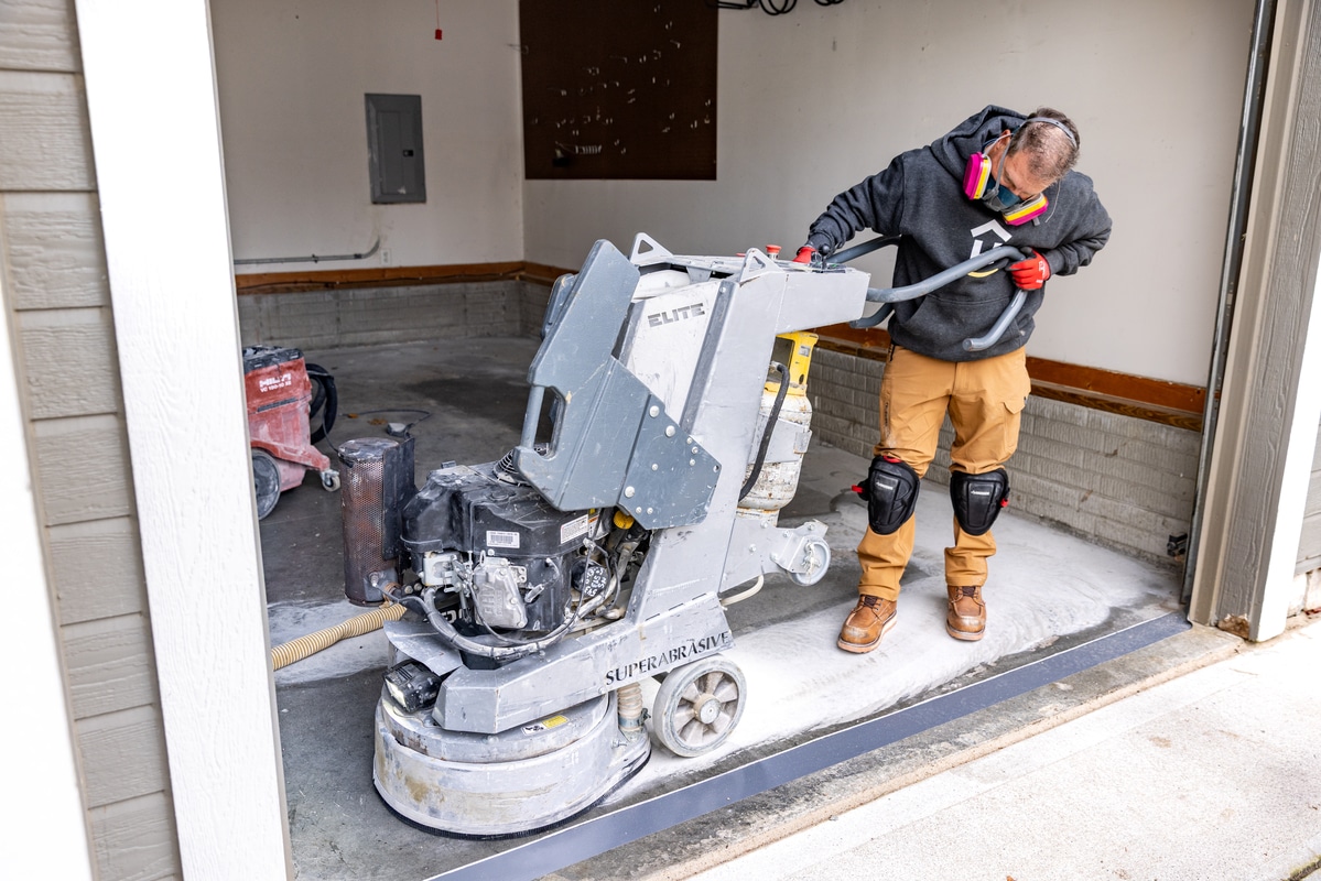 Garage Flooring Installer running a diamond grinder to grind down the concrete for a coating